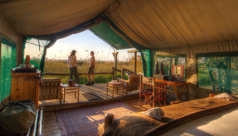 Couple standing on private viewing deck in safari tent at Camp Xakanaxa