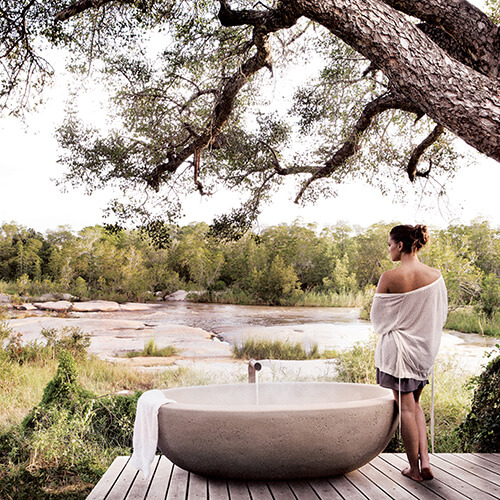 Woman standing next to outdoor pool on private deck at Londolozi private granite suites