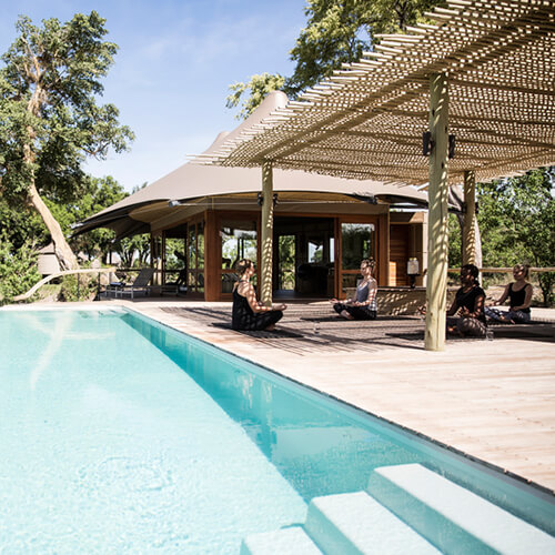 Women doing yoga next to the pool at Mombo Camp in Botswana