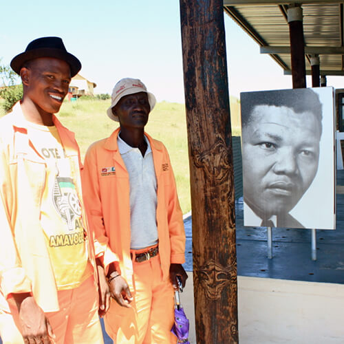 Two men stand next to a picture of Nelson Mandela at the Nelson Mandela Museum in Mvezo